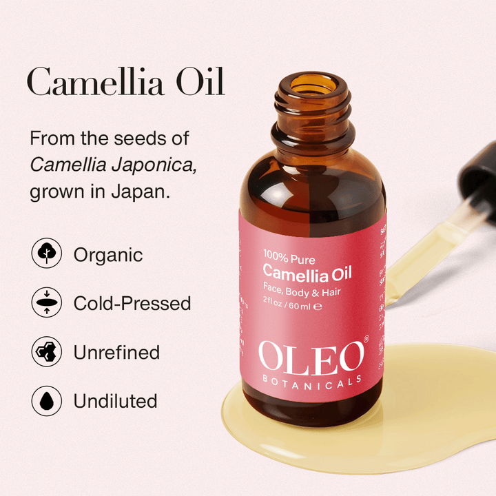 Amber glass bottle of Oleo Botanicals 100% Pure Camellia Oil with pink label, surrounded by spilled oil and dropper. Cold-pressed, unrefined, organic, and undiluted from Camellia Japonica seeds grown in Japan.